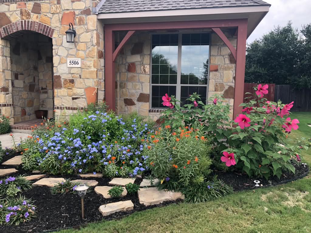 An established front bed in full bloom with a flagstone path and steel edging.